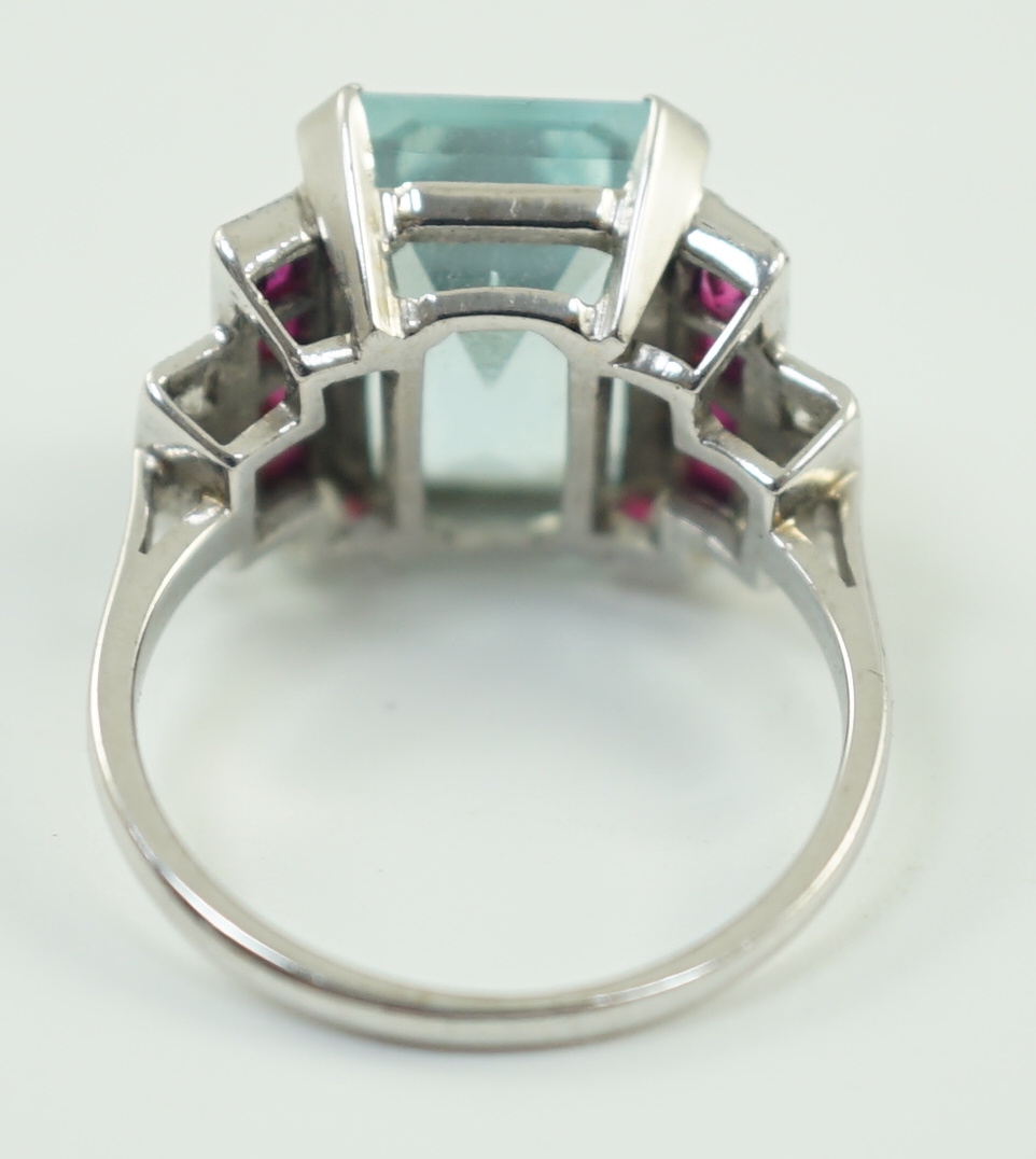 A platinum and single stone emerald cut aquamarine set dress ring, with ruby and diamond set stepped shoulders